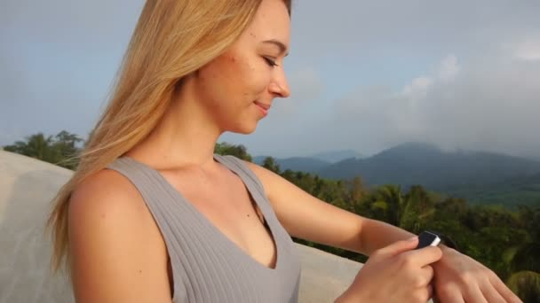 Chica entrenadora de fitness de cámara lenta probando smartwatch en el balcón del hotel — Vídeos de Stock