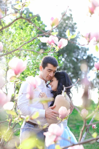 Morena menino feliz abraçando e beijando menina caucasiana perto de magnólia . — Fotografia de Stock