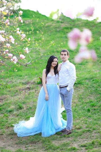 Jovem mulher bonita vestindo vestido azul e andando perto de magnólia com namorado . — Fotografia de Stock