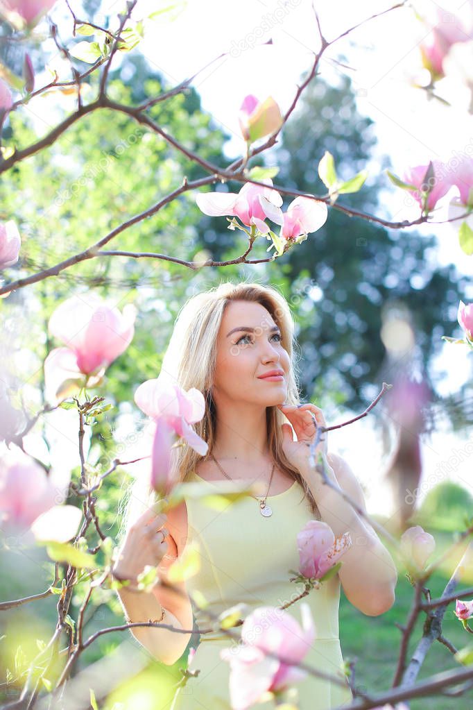 Young dreaming woman standing near magnolia in park.