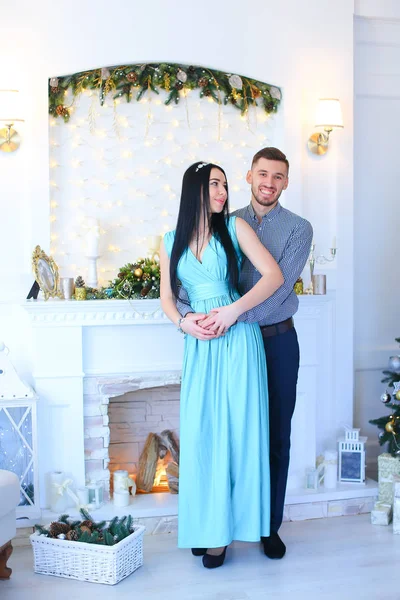 Mulher vestindo vestido de pé com o marido perto de lareira e árvore de Natal . — Fotografia de Stock