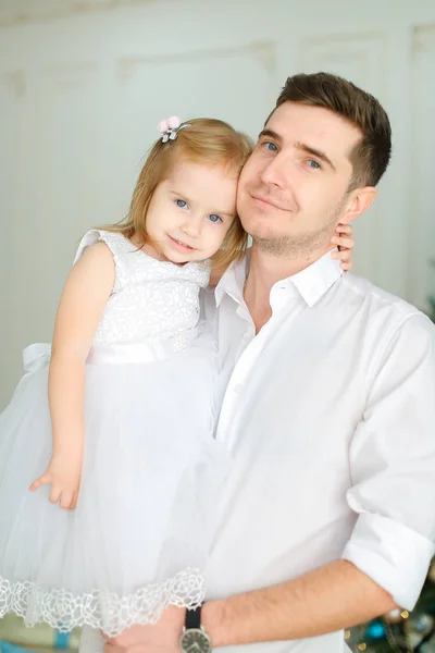 Joven padre caucásico manteniendo pequeña hija vistiendo vestido blanco . — Foto de Stock