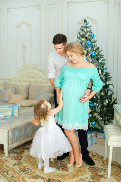 W ciąży kobieta osoby noszącej stojący sukienka z mężem i córeczką w pobliżu choinki. — Zdjęcie stockowe
