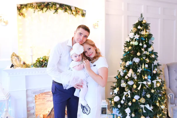 Jovem mãe e pai mantendo pouco bebê feminino perto da árvore de Natal e lareira decorada . — Fotografia de Stock