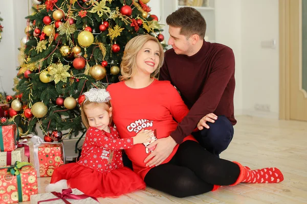 Sorrindo mulher grávida sentada com marido e filha perto de presentes sob a árvore Chistma . — Fotografia de Stock