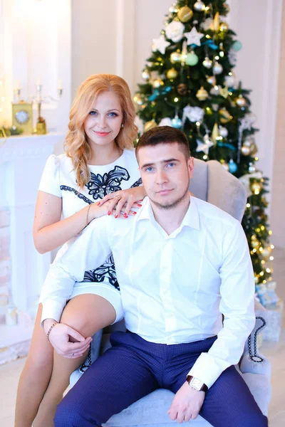 Noel ağacı yakınındaki beyaz gömlek giymiş kocasıyla birlikte oturan genç karısı.