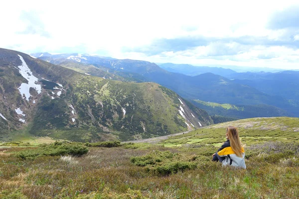 Kadın turist üzerinde sarı ceket, oturma ve Alp Dağları üzerinde seyir.