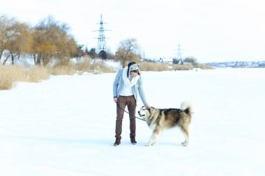 Kazak, kahverengi etek giyen adam ve kar üzerinde oturan ve sarılma mittens husky köpek.