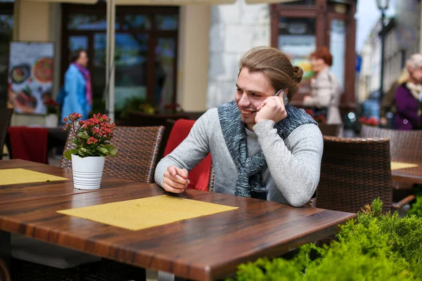 Joven hombre caucásico sentado en el café sreet y hablando por teléfono inteligente . — Foto de Stock