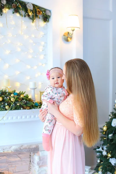 Genç kadın uzun saçlı kadın çocuk kollarında tutarak ve dekore edilmiş şömine ve Noel ağacı ayakta.