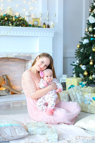 Pembe elbise giyen genç anne holding kız omuz omuza yakın bir şekilde dekore edilmiş şömine ve Noel ağacı,.