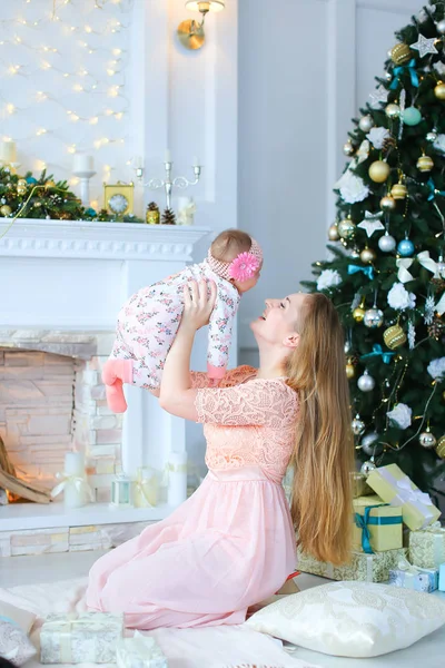 Pembe elbise giyen genç kadın holding kızı omuz omuza yakın bir şekilde dekore edilmiş şömine ve Noel ağacı,.