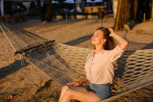 Genç Amerikalı sarışın kadın beyaz hasır hamakta kum üzerinde dinlenme.