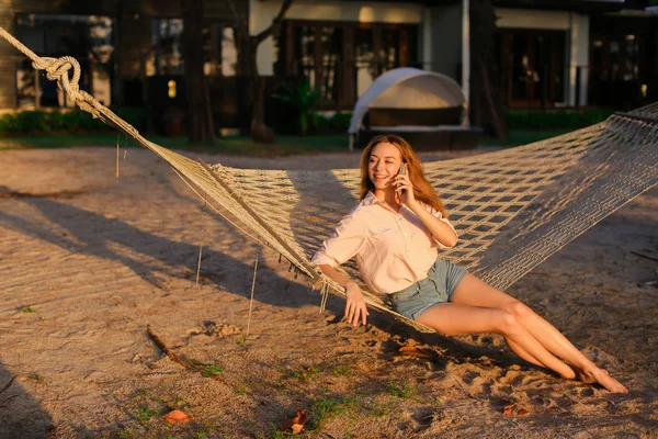 Hamakta oturmuş ve smartphone, yaz tatillerini konuşan genç kadın.