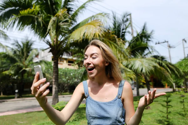 Joven mujer feliz haciendo selfie por teléfono inteligente con palmas en el fondo . — Foto de Stock