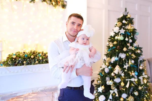 Jovem pai mantendo pouco bebê feminino perto da árvore de Natal e lareira decorada . — Fotografia de Stock