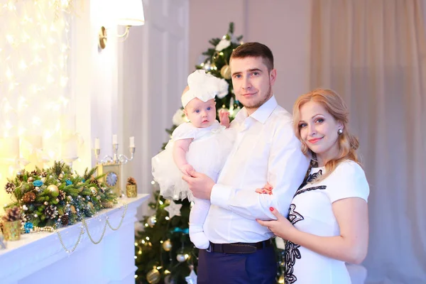 Young parents keeping little female baby near Christmas tree in background. — Stock Photo, Image
