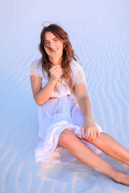 Plaj beyaz kum üzerinde oturan ve elbise gülümseyen kadın.