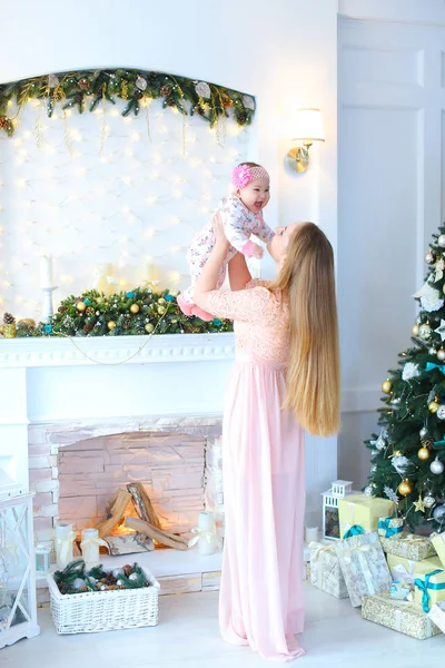 Kadın çocuk kollarında tutarak ve dekore edilmiş şömine ve Noel ağacı yakın duran genç anne.