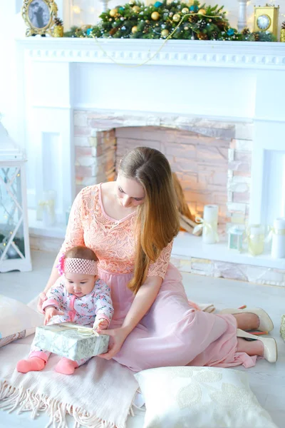 Jovem mãe presenteando pequena filha presente perto de lareira decorada . — Fotografia de Stock