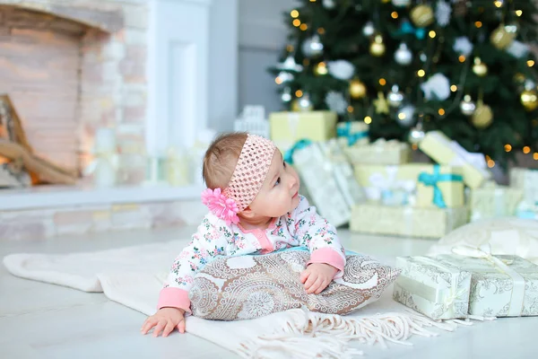 Hübsches weibliches Baby liegt auf dem Boden neben funkelndem Weihnachtsbaum und Geschenken. — Stockfoto