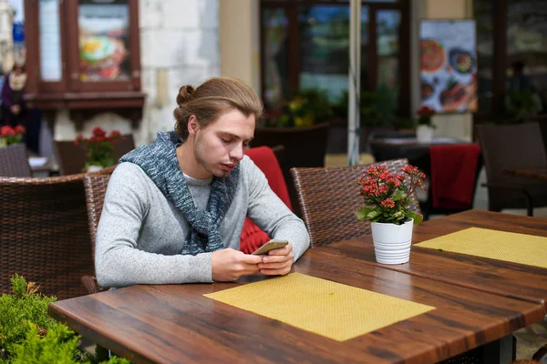 Joven sentado en la cafetería sreet y charlando por teléfono inteligente . — Foto de Stock