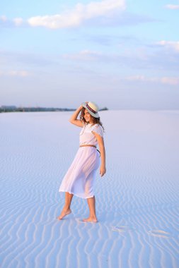 Genç beyaz kız beyaz elbise ve şapka üzerinde kum barefo gidiyor