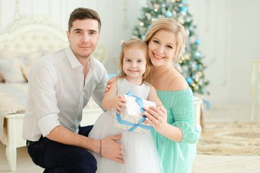 Mutlu kadın ve küçük kızı Noel ağacı içinde arka plan mevcut, tutmak ile oturan adam.