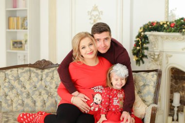 Küçük kızı ile Divan dekore edilmiş şömine yakın oturan hamile anne ve baba.