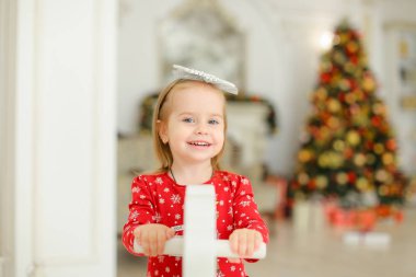 Sallanan at, arka plan bulanık Noel ağacı ile oynarken küçük gülümseyen kız.