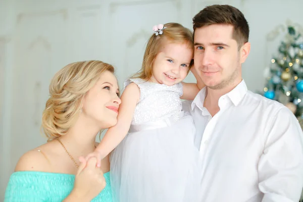 Schöner Vater hält kleine Tochter und junge Mutter beim Händeküssen am Weihnachtsbaum. — Stockfoto