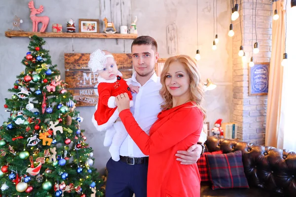 Junge blonde Frau und Mann stehen mit weiblichem Baby neben Weihnachtsbaum. — Stockfoto
