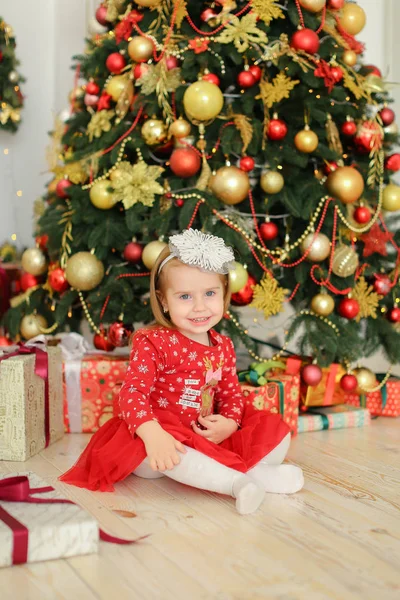 Junge Mutter trägt weißes Kleid und hält kleines weibliches Baby in der Nähe des Weihnachtsbaums. — Stockfoto