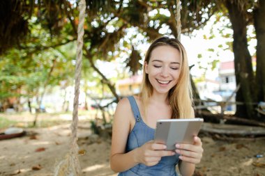 Kot sundress tablet kullanma ve salıncak kum üzerinde sürme genç Amerikalı kız giyiyor.