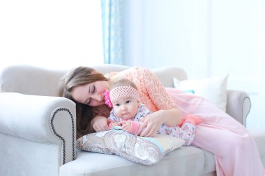 Çocuk ile kanepede oturan ve pembe elbise giyen genç beyaz anne.