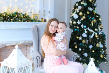 Genç Anne holding bebek büyüleyici ve fenerler, şömine ve Noel ağacı yakınındaki kanepede oturan.