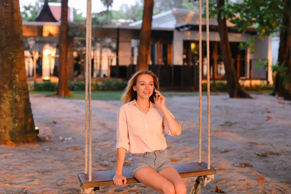 Smartphone ile konuşmak ve oturan genç kafkas kadın salıncak, arka planda kum.