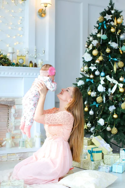 Pembe elbise giyen genç mutlu anne holding kız omuz omuza yakın bir şekilde dekore edilmiş şömine ve Noel ağacı,.