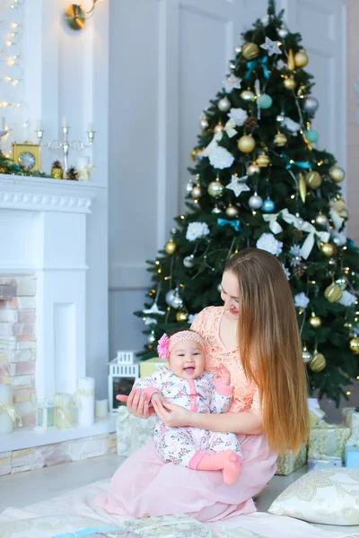 Pembe elbise gülümseyen kadın holding kızı omuz omuza yakın bir şekilde dekore edilmiş şömine ve Noel ağacı,.