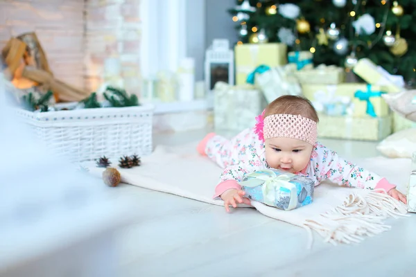 Jolie bébé femelle couchée sur le sol sur une couverture avec un cadeau près de l'arbre de Noël scintillant . — Photo