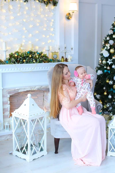 Kadın bebek ve beyaz fener yakınındaki kanepede oturan, dekore edilmiş şömine ve Noel ağacı tutan genç beyaz anne. Kutluyor kış tatilleri ve annelik kavramı.