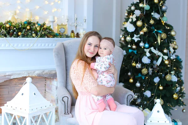 Genç Anne holding bebek büyüleyici ve fenerler, şömine ve Noel ağacı yakınındaki kanepede oturan.