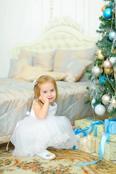 Lilla kaukasiska flicka sitter nära presenterar under julgranen i sovrum. — Stockfoto