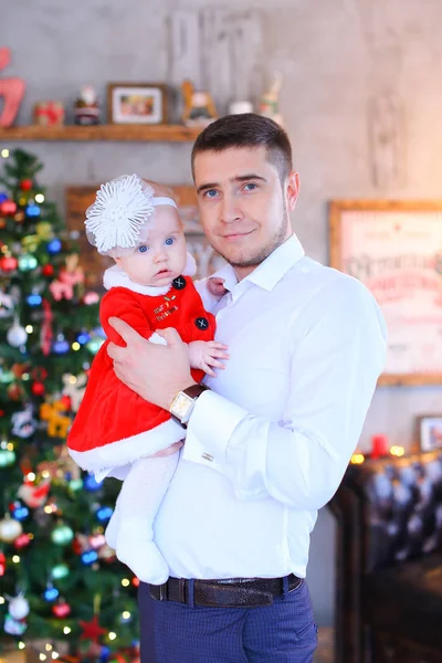 Junger Vater hält kleine Tochter in Weihnachtsbaumnähe im Hintergrund. — Stockfoto