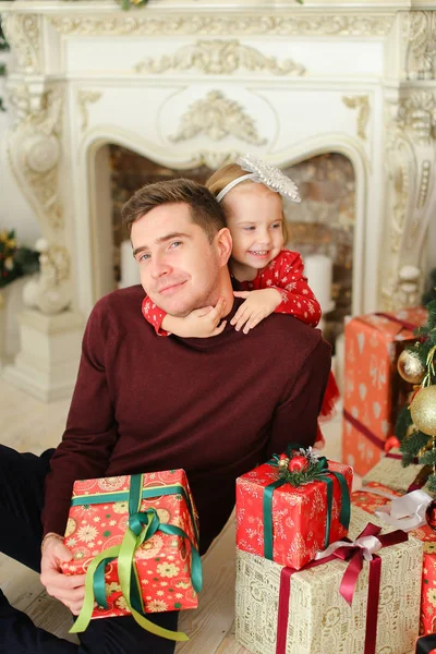 Pai caucasiano sentado com a pequena filha perto de lareira decorada e mantendo presentes . — Fotografia de Stock