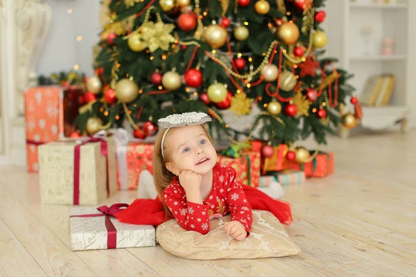 Petite fille heureuse portant une robe rouge couchée près du sapin de Noël et des cadeaux . — Photo