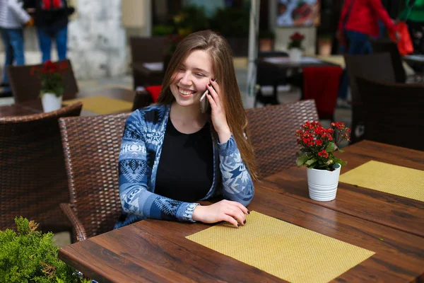 スマート フォンで赤い花近くのカフェで話している若い女性. — ストック写真