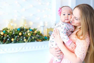 Bir şekilde dekore edilmiş şömine duran ve küçük kızını tutan genç anne.