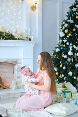 Pembe elbise giyen genç ptretty anne holding kız omuz omuza yakın bir şekilde dekore edilmiş şömine ve Noel ağacı,.