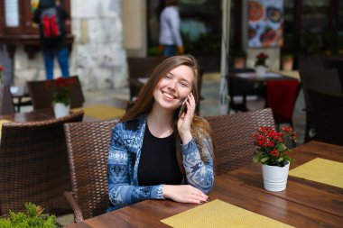 Genç beyaz kadın kırmızı çiçekler yakınındaki kafede Smartphone tarafından söz.